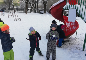 Trzech chłopców bawi się śnieżkami w ogrodzie przedszkolnym.